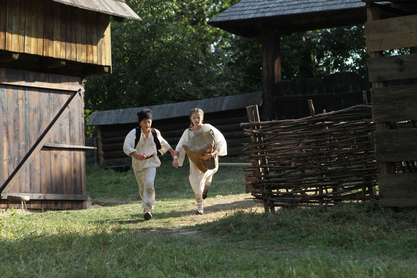 Two children in traditional costume running among the wooden buildings of a village