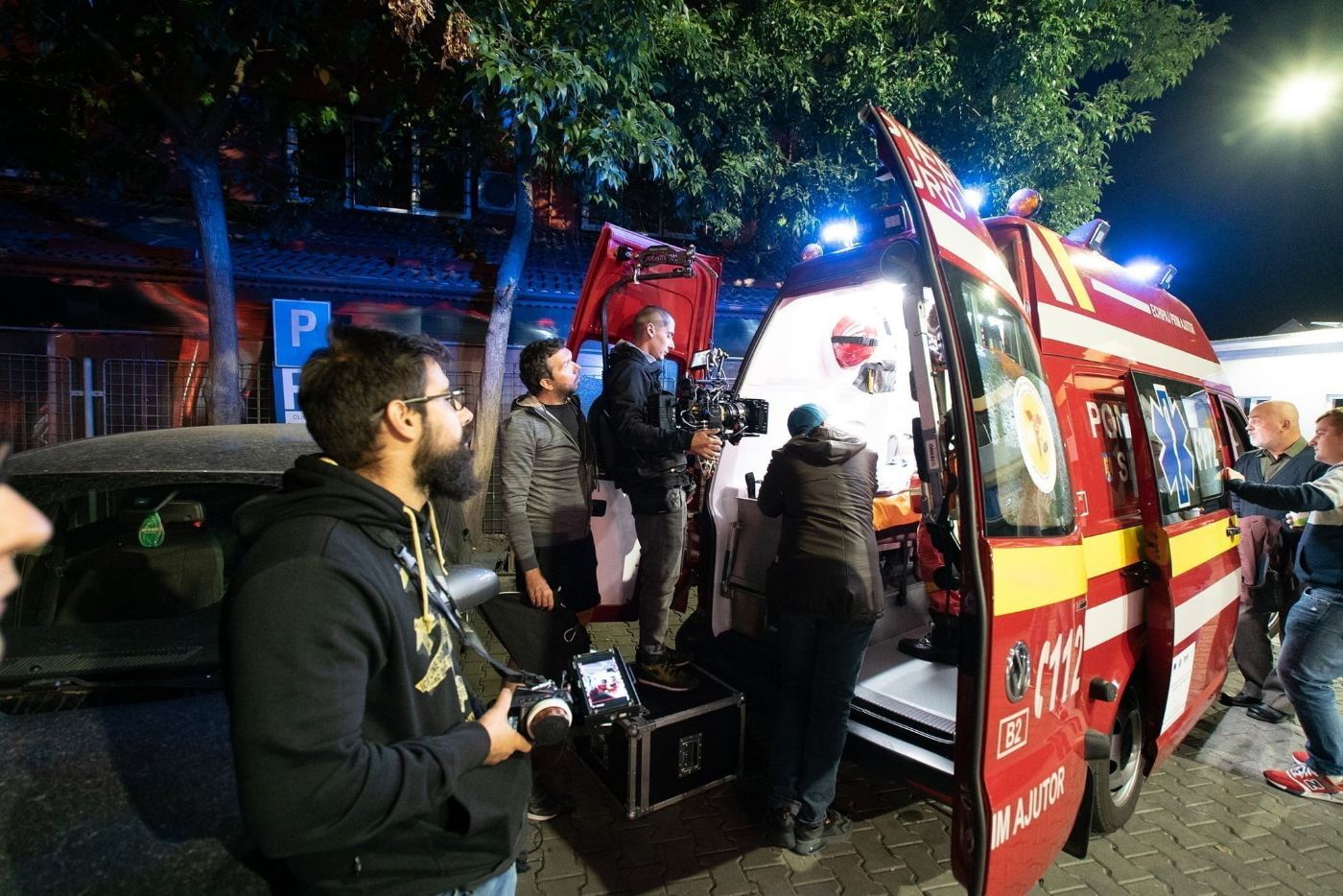 The crew filming at night beside an ambulance with its lights flashing