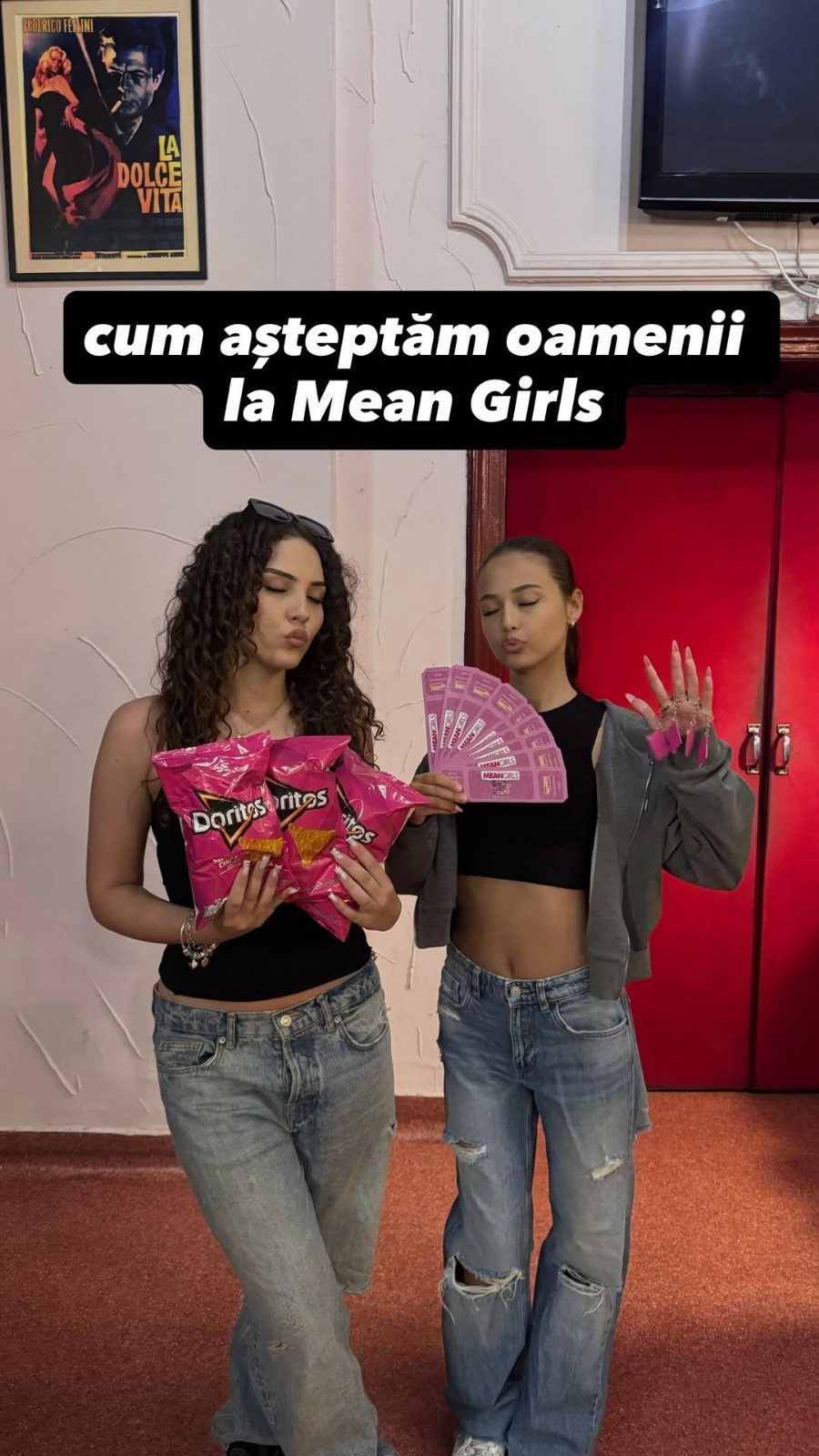 Două voluntare cu bilete și snacksuri roz, în foaierul cinematografului.