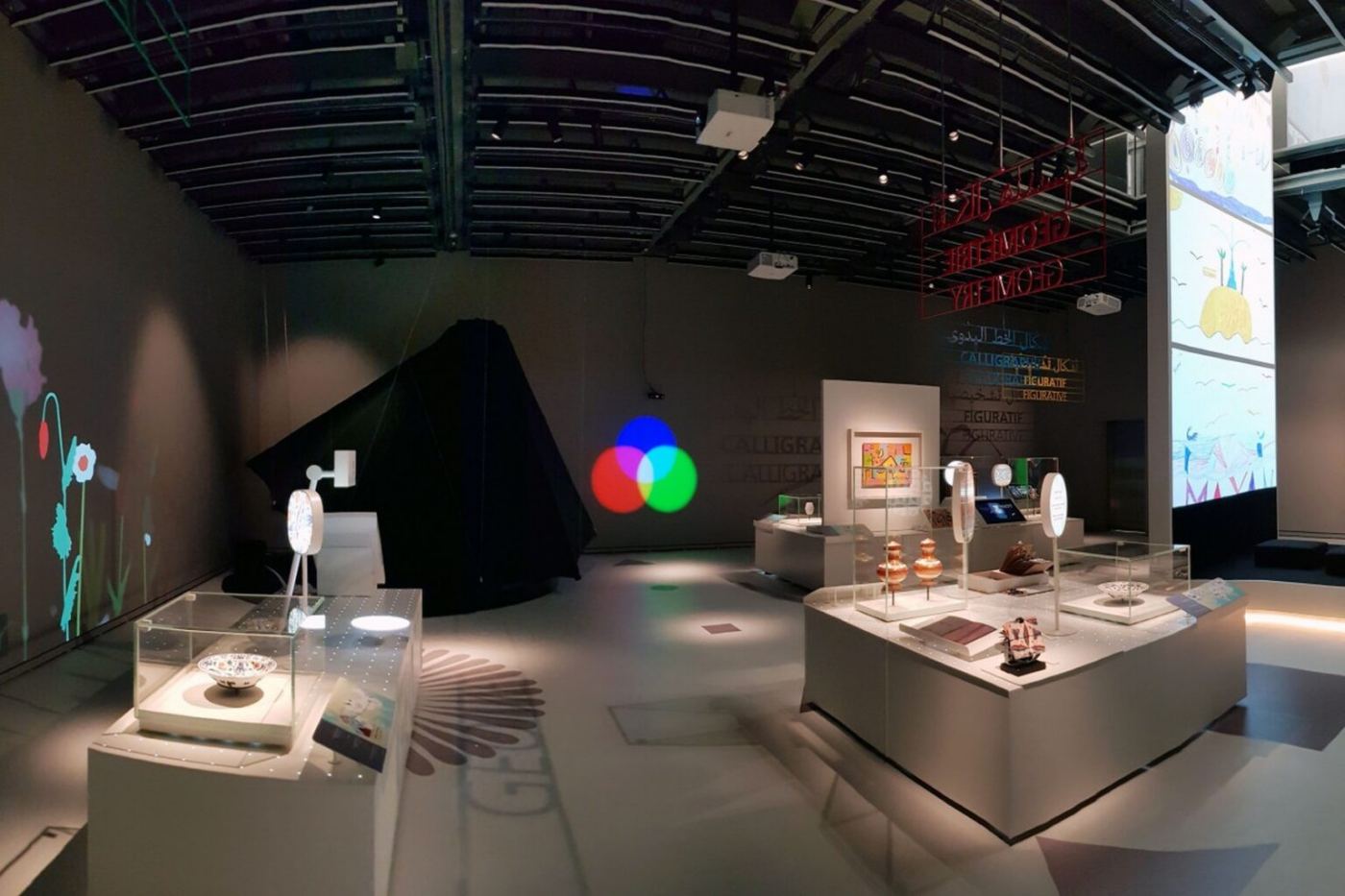A wide view of the exhibition, with display cases, projections and coloured shapes