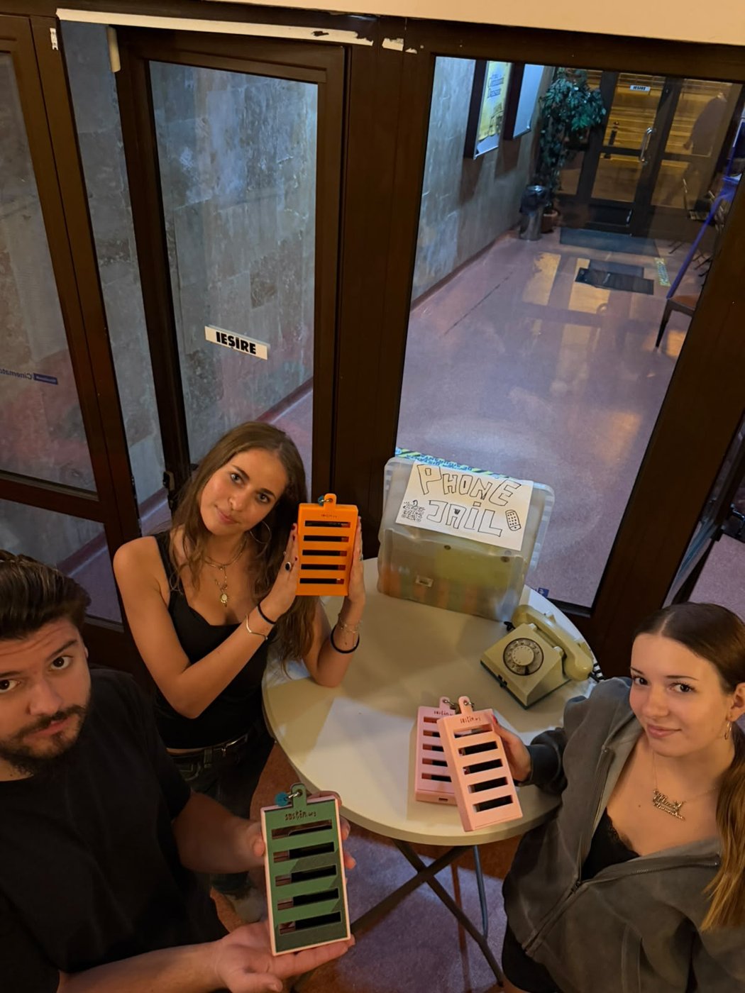 Three team members with coloured phone jails, around the table in the foyer.