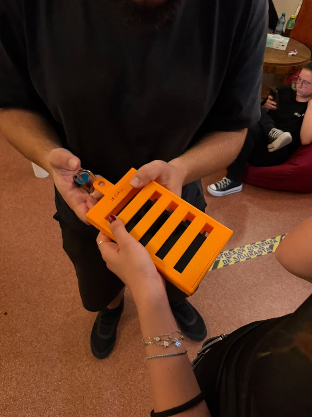 An orange 3D-printed phone jail, with padlock and key, held in someone's hands.