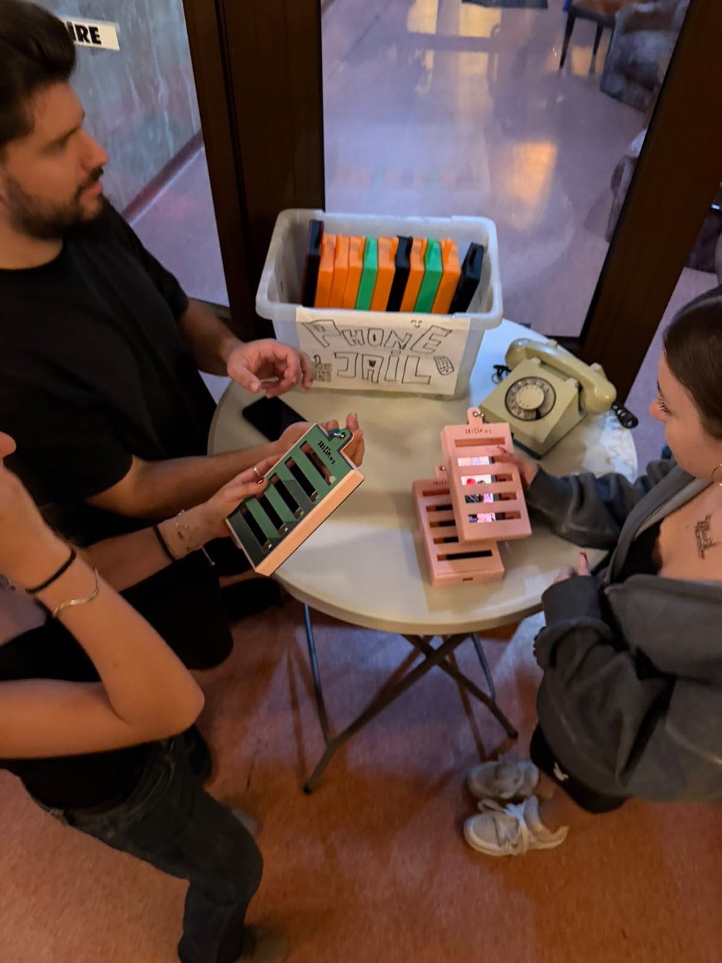The “Phone Jail” box full of coloured cases, on the table at the auditorium door.