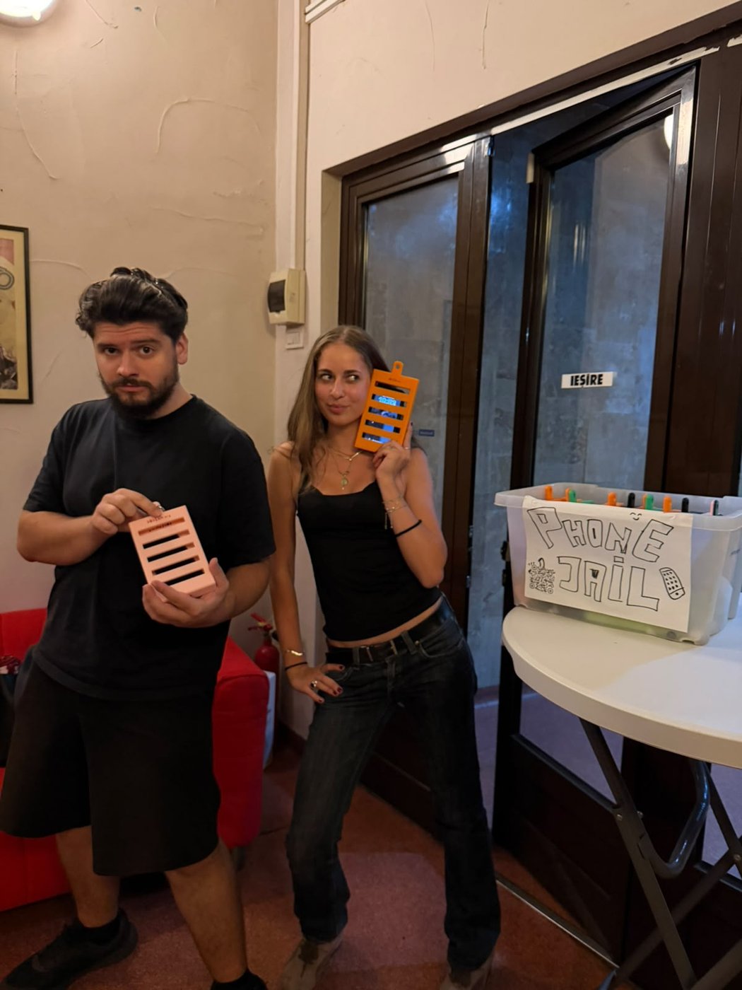 Two volunteers holding 3D-printed phone jails, next to the “Phone Jail” box in the Cinema Europa foyer.